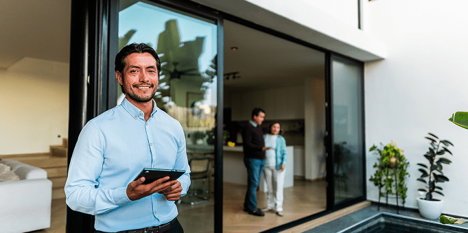 Smiling man holding tablet outside modern home.